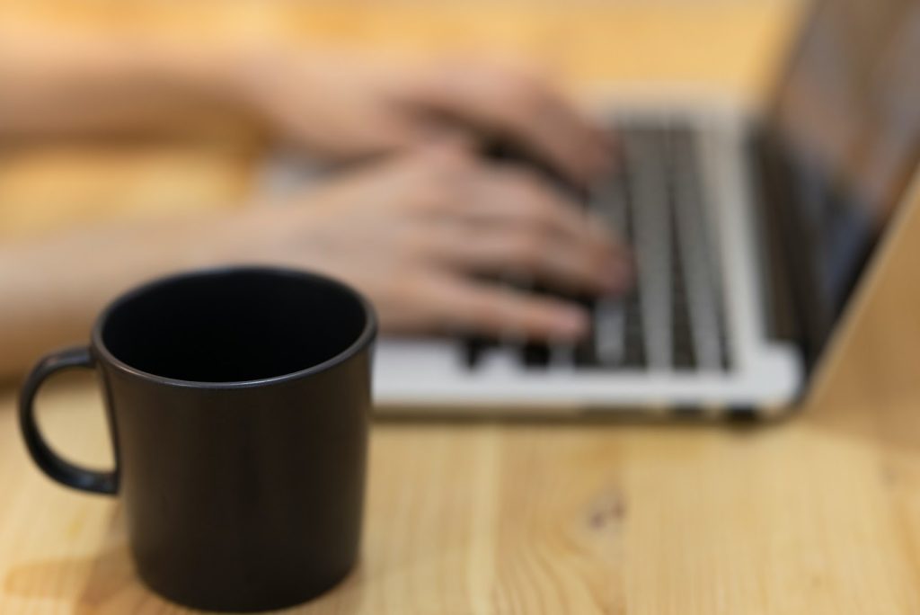 A guy writes on a laptop with a mug of coffee, but the laptop is blurred for security