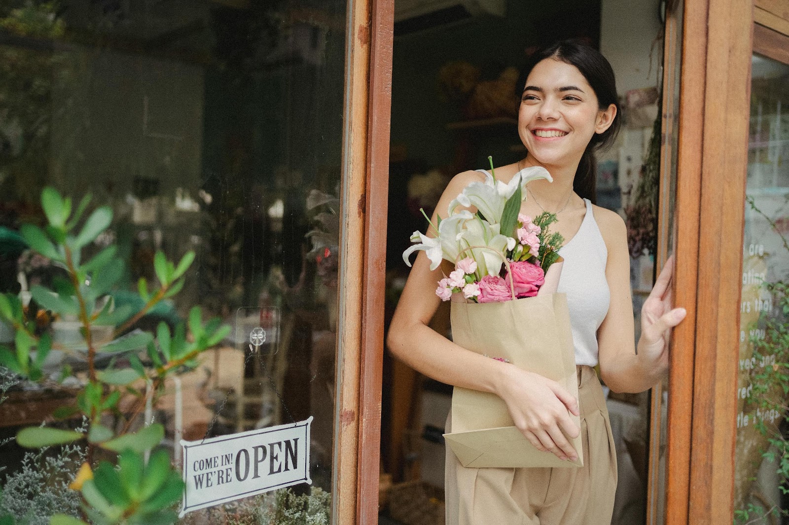 Young woman leaves a small business through the front door holding a bag of fresh-cut flowers.